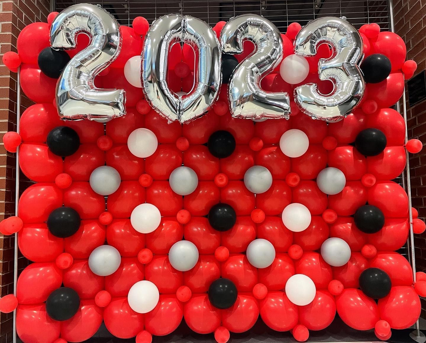 A wall made of red , white , and black balloons with the year 2023 written on it.