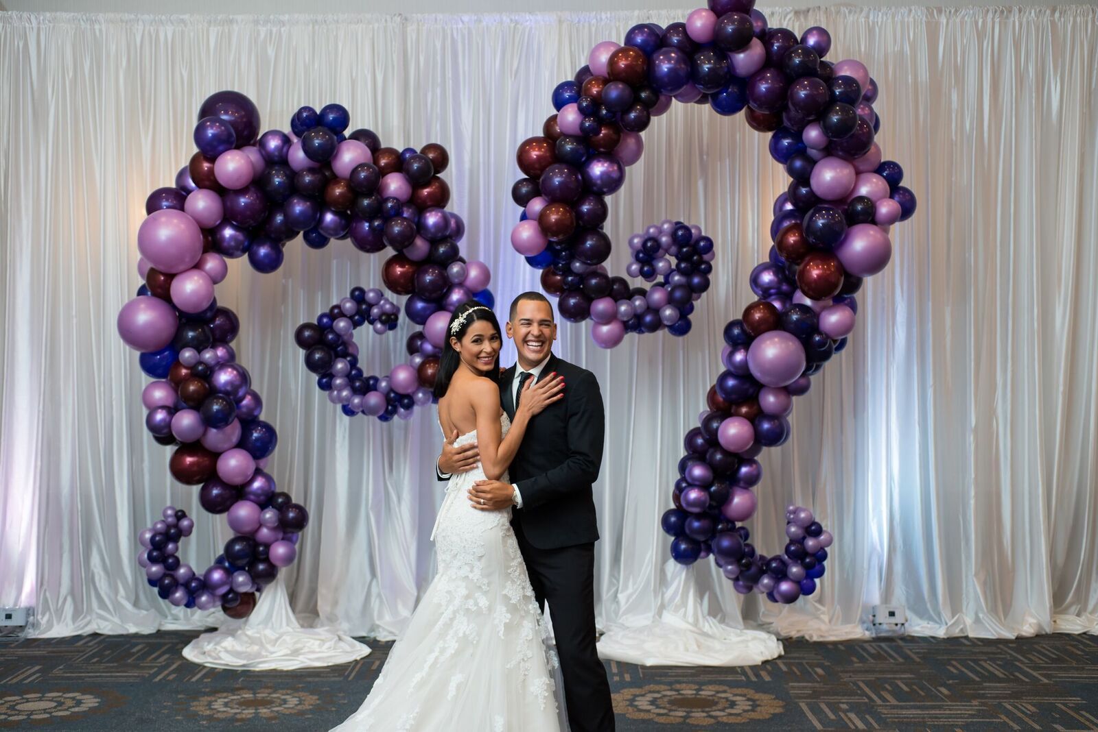 A bride and groom are posing for a picture in front of a balloon sculpture.