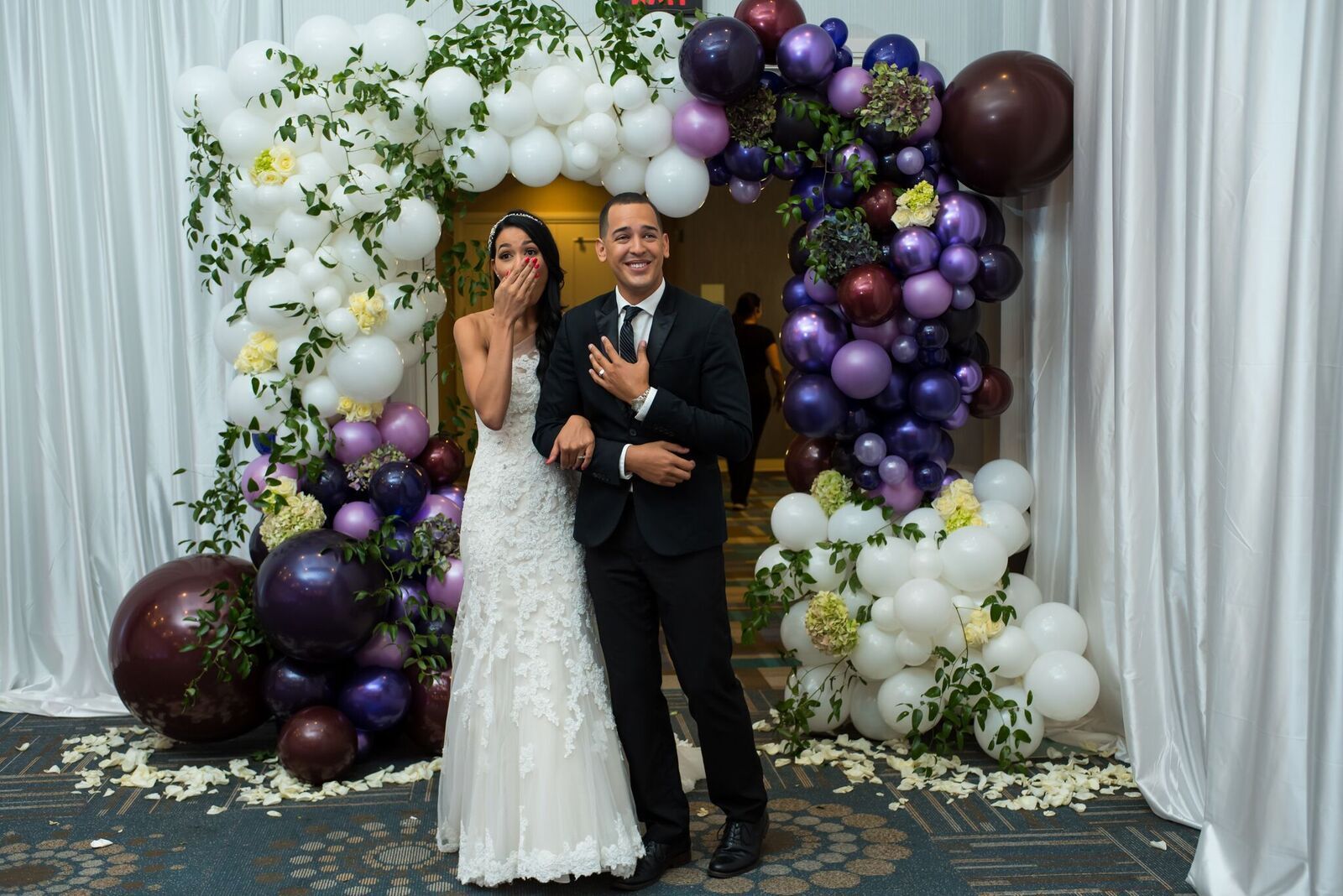 A bride and groom are posing for a picture in front of a balloon arch.