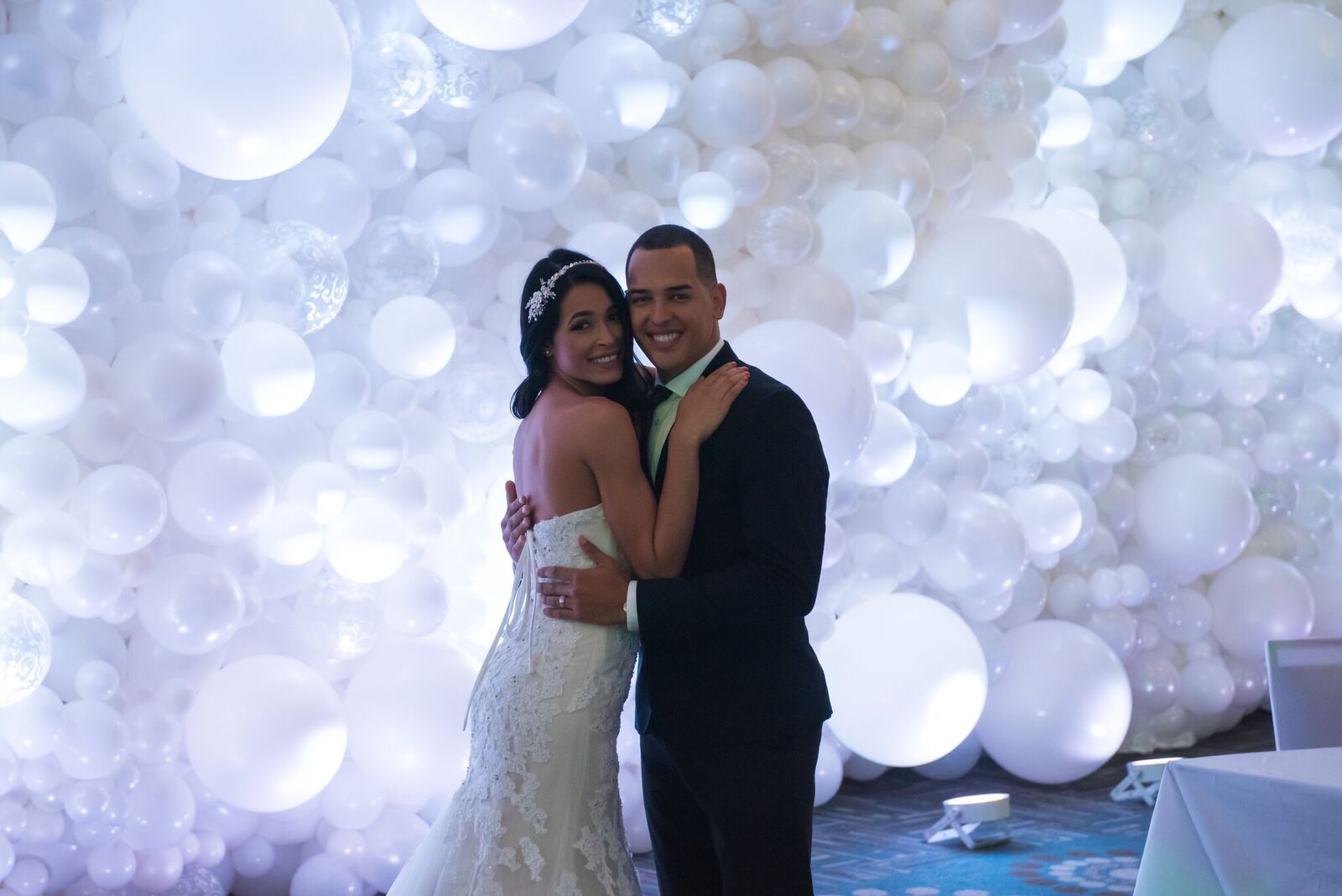 A bride and groom are posing for a picture in front of a wall of white balloons balloons.