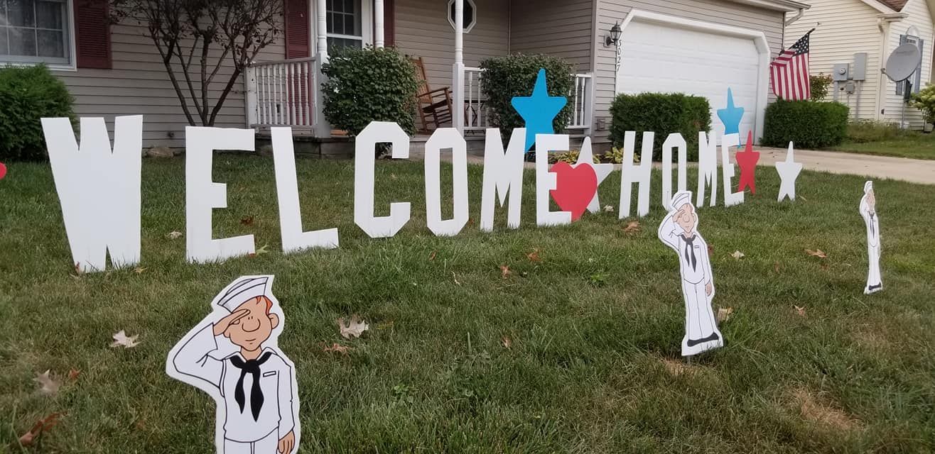 A welcome home sign is in front of a house. Navy themed yard card
