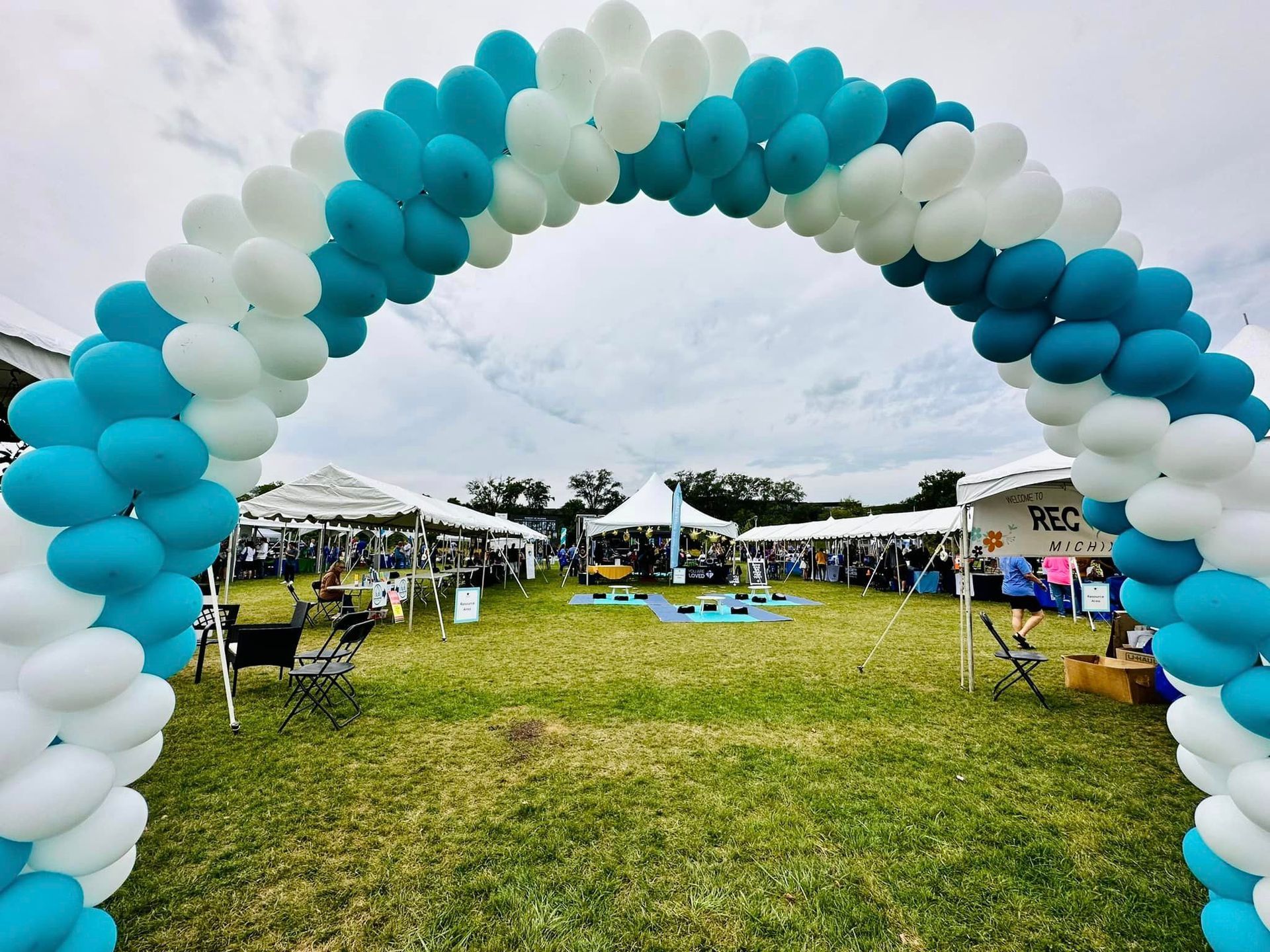 A blue and white balloon arch is in the middle of a field.