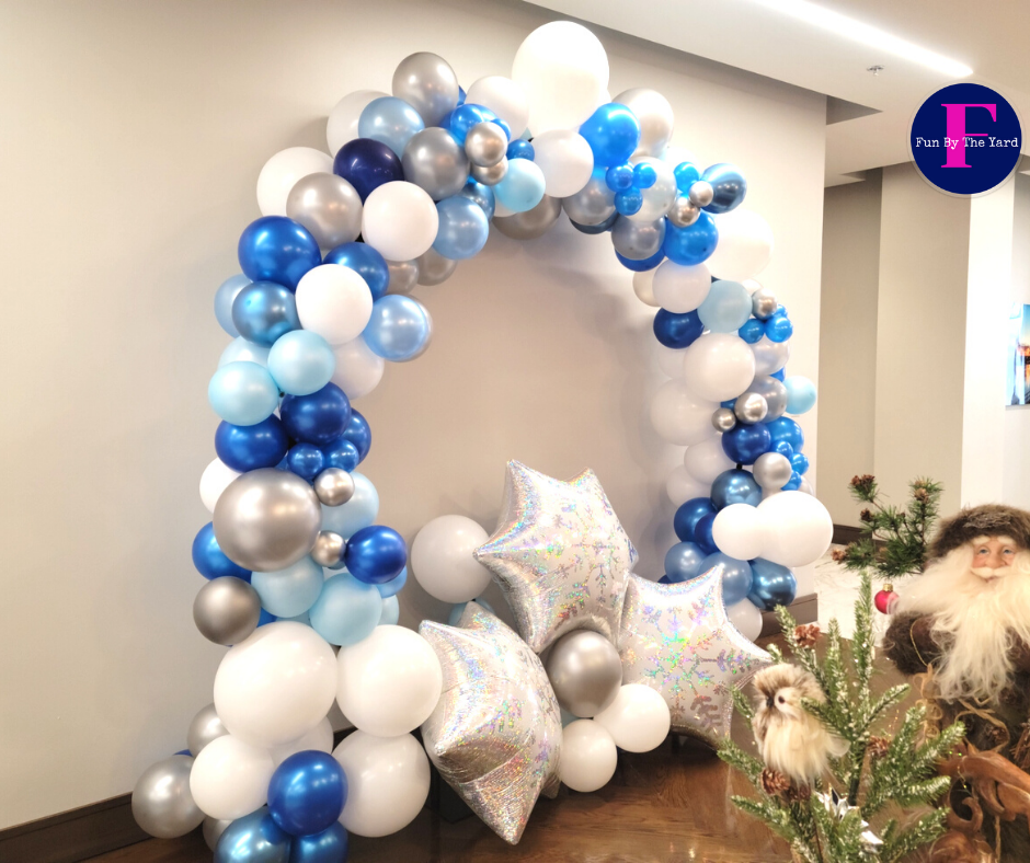 A balloon arch with blue , white , and silver balloons in a room.