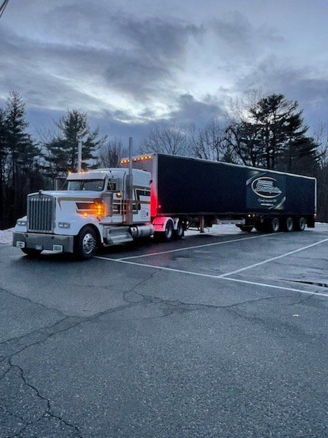 Un semi-remorque blanc avec une remorque noire est stationné sur un parking au crépuscule.