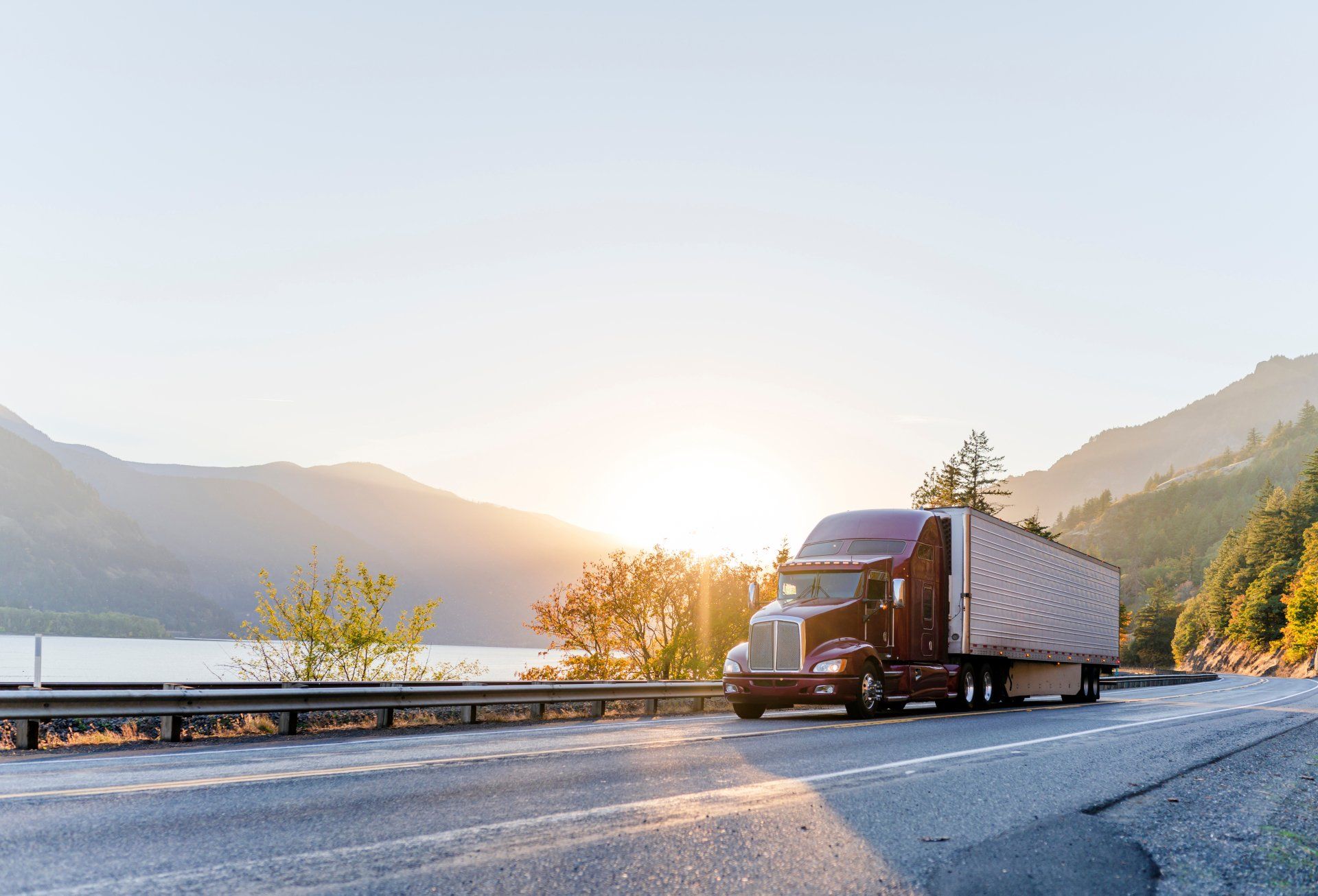 Un semi-camion roule sur une autoroute à côté d'un lac au coucher du soleil.