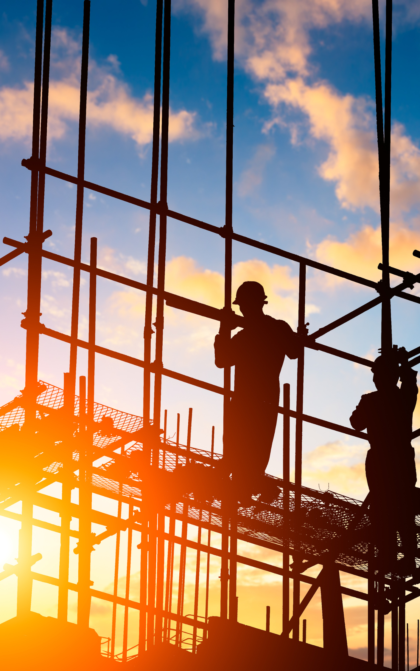 Two construction workers are standing on scaffolding at a construction site at sunset.