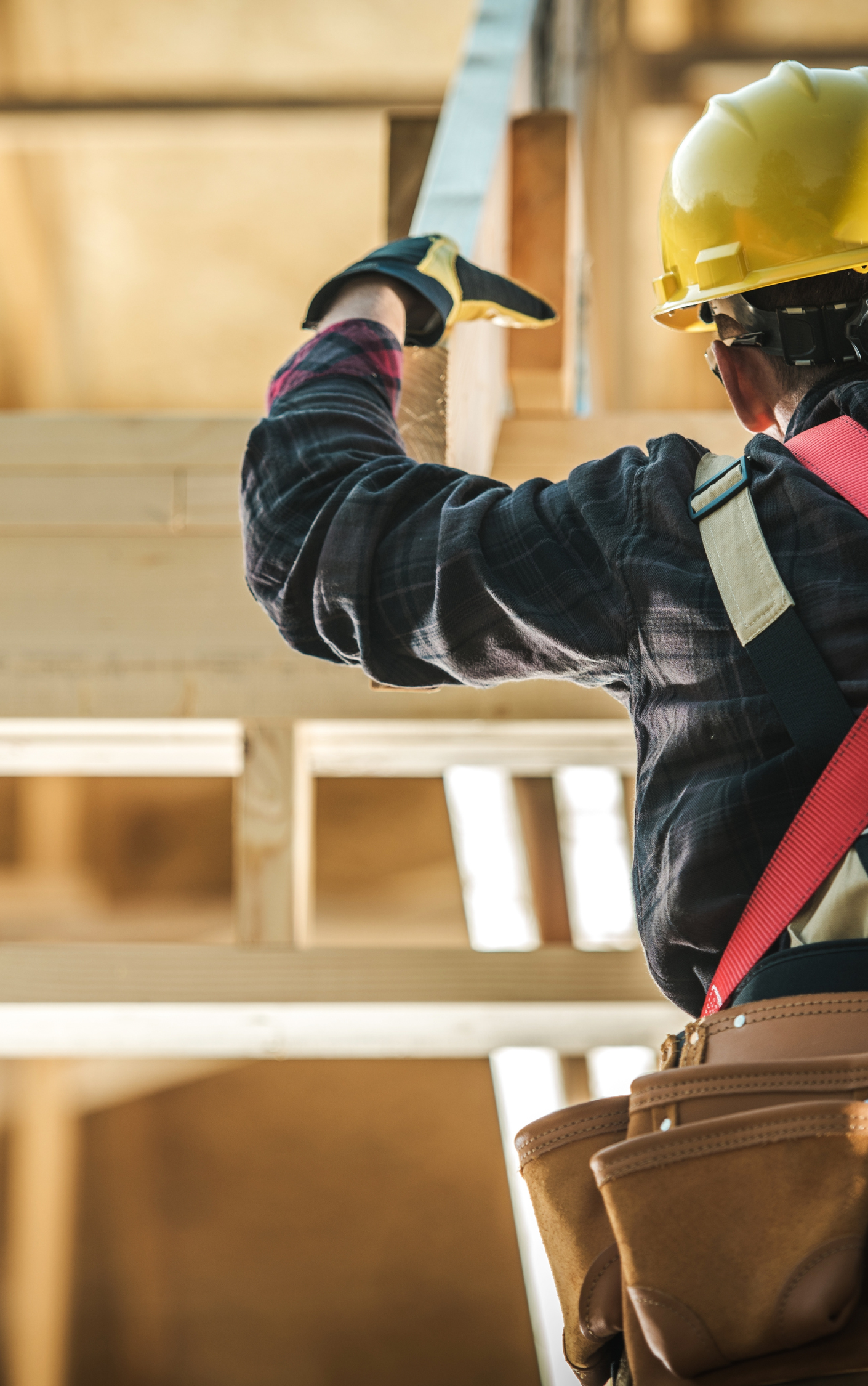 A construction worker wearing a hard hat and gloves is working on a wooden structure.