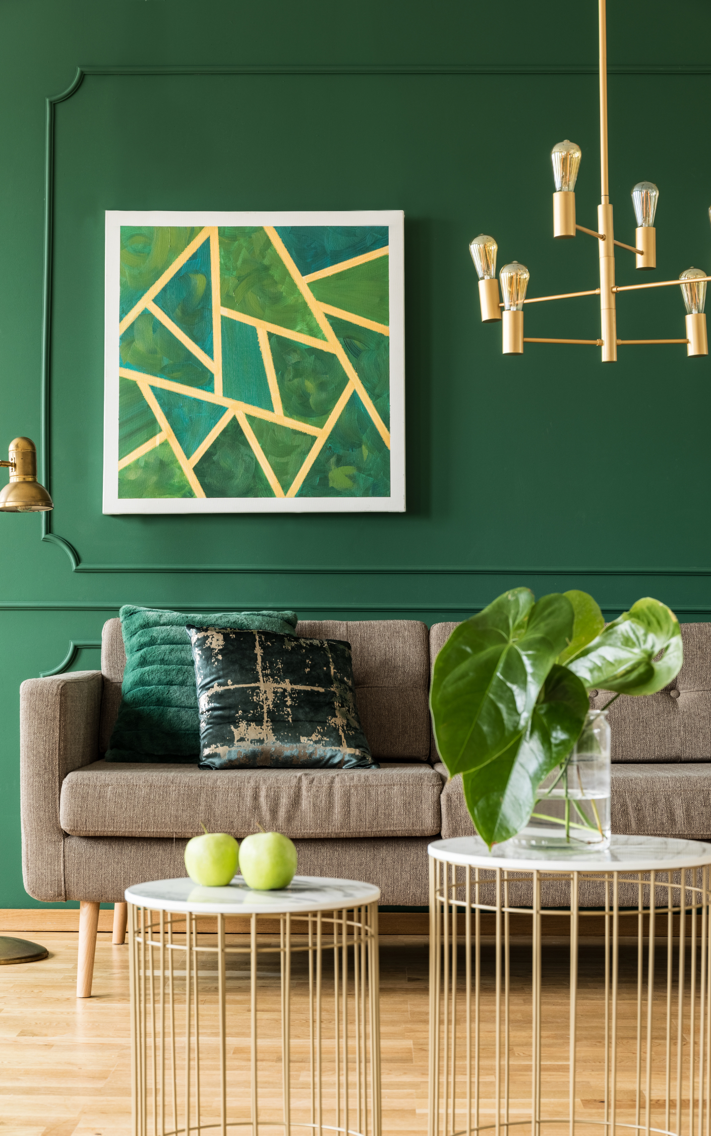 A living room with green walls , a couch , two tables and a chandelier.
