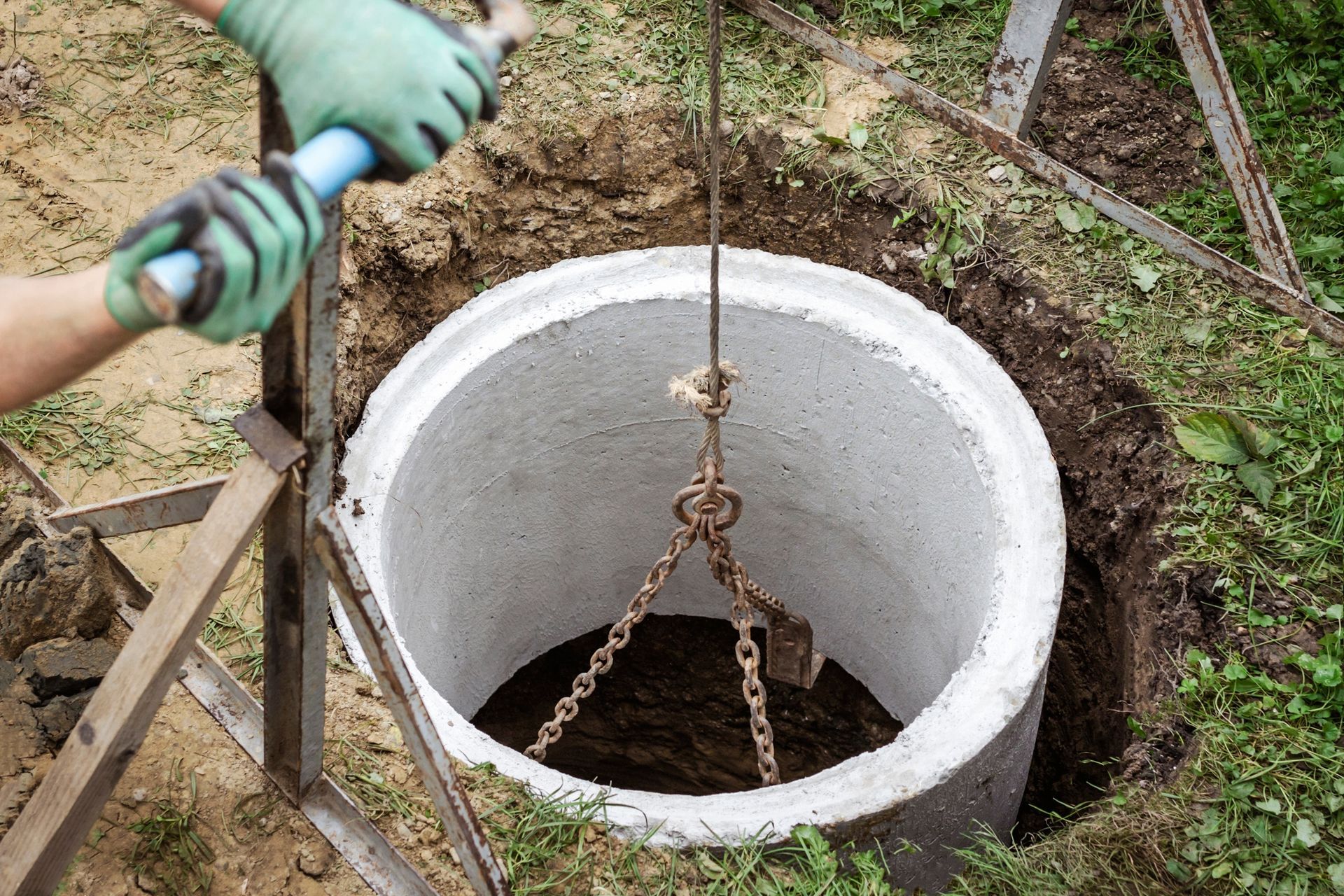 A man is using a crane to lift a concrete ring into the ground.