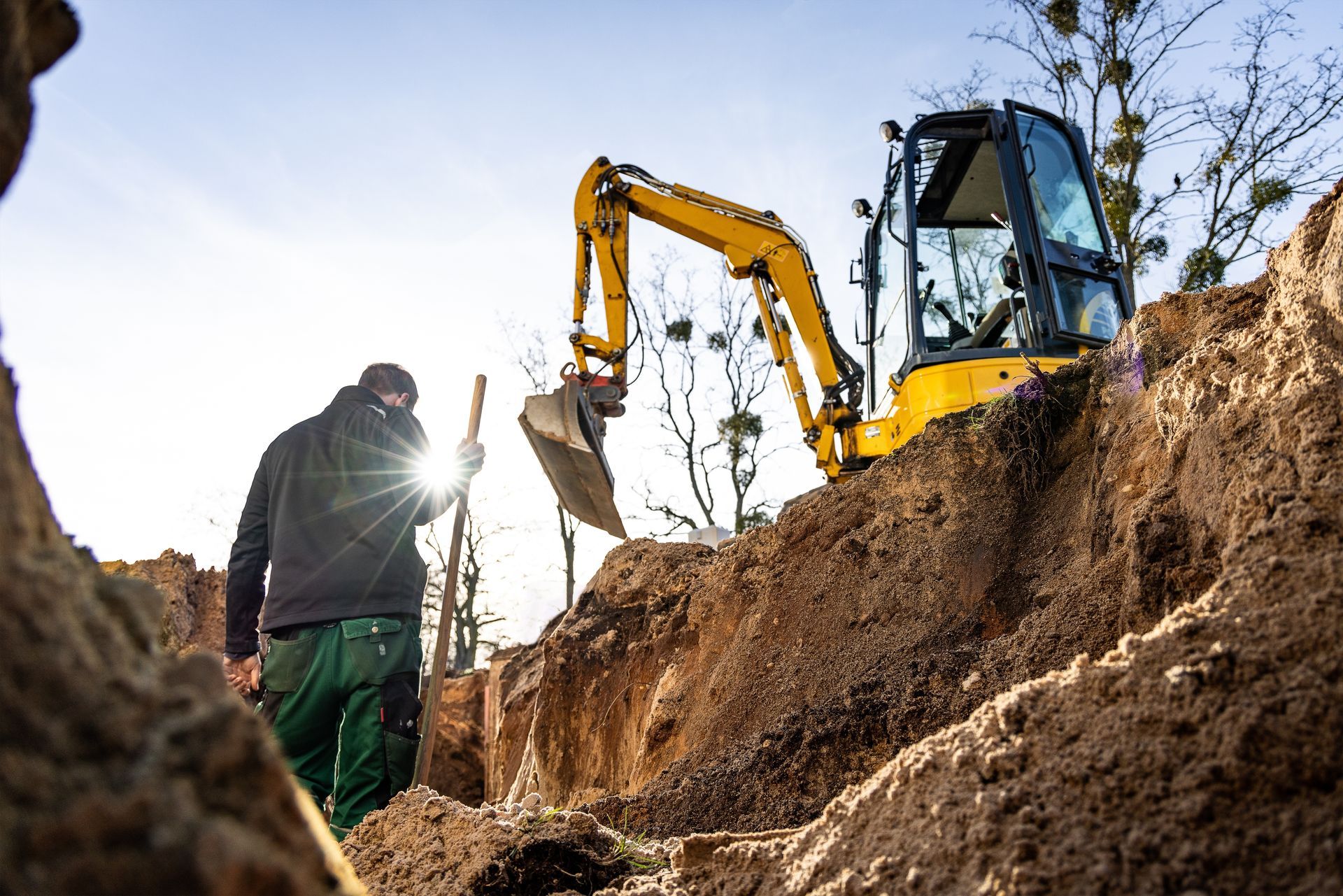 A man is digging in the dirt next to a yellow excavator.