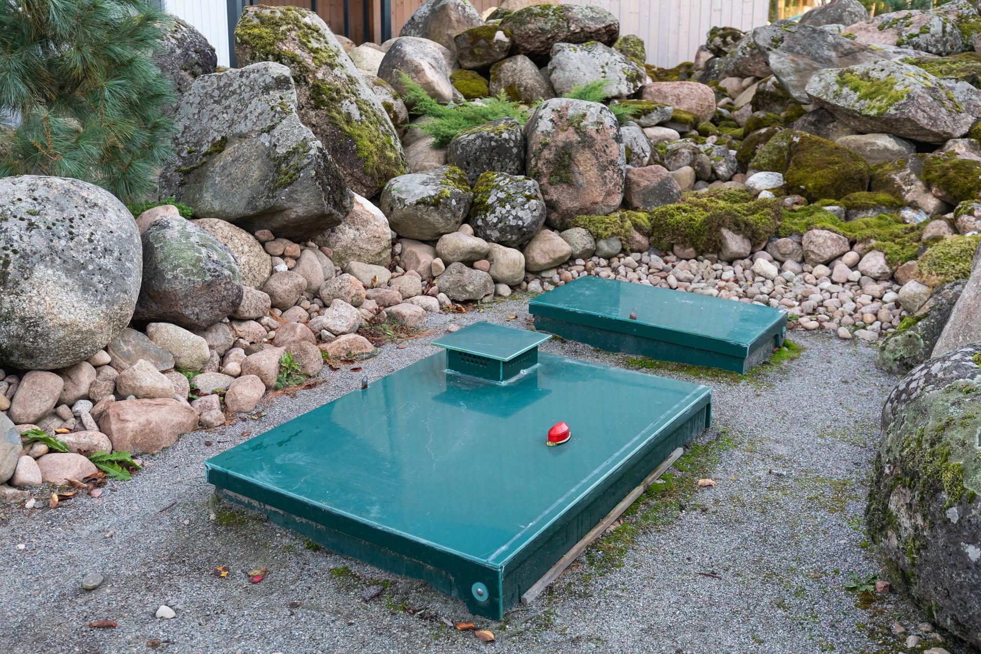 A green septic tank is sitting in the middle of a rocky area.