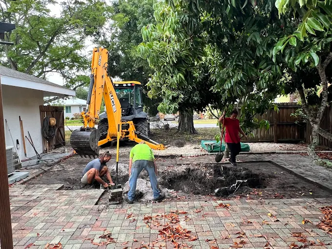 A group of construction workers are digging a hole in a backyard.