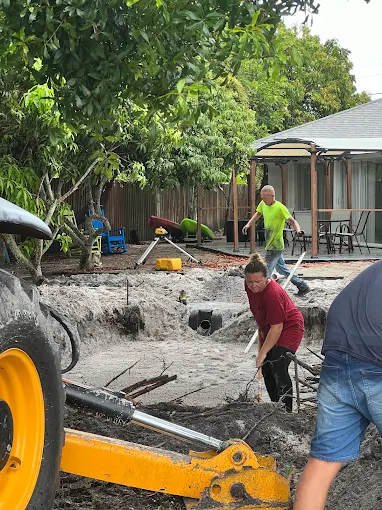 A group of people are digging in the dirt in front of a house.