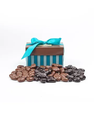 A blue and brown striped box filled with chocolate covered almonds next to a pile of chocolate covered almonds.