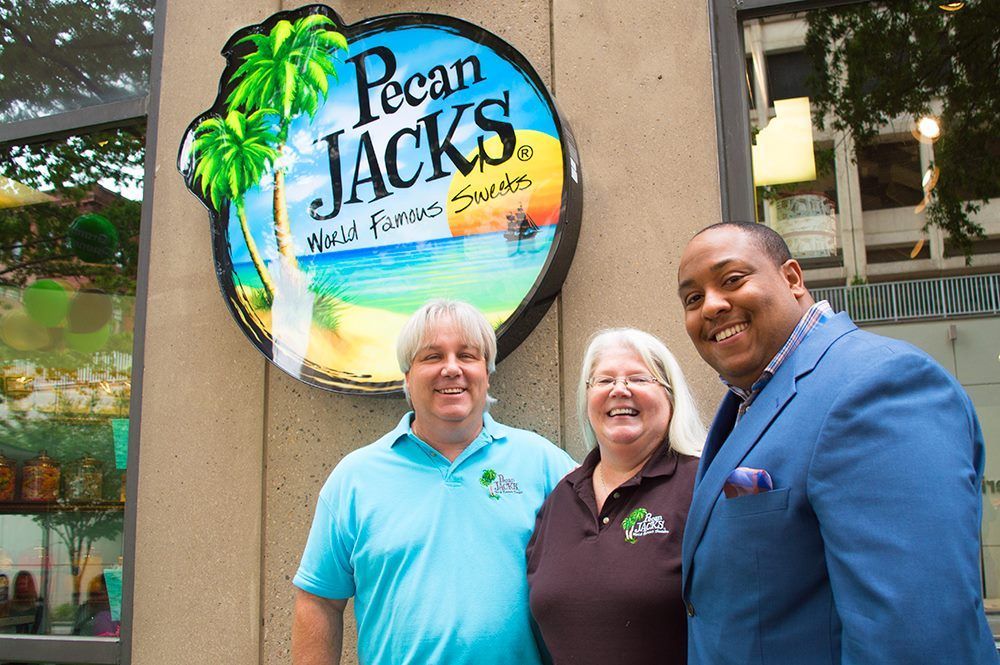 Three people standing in front of a pecan jacks sign
