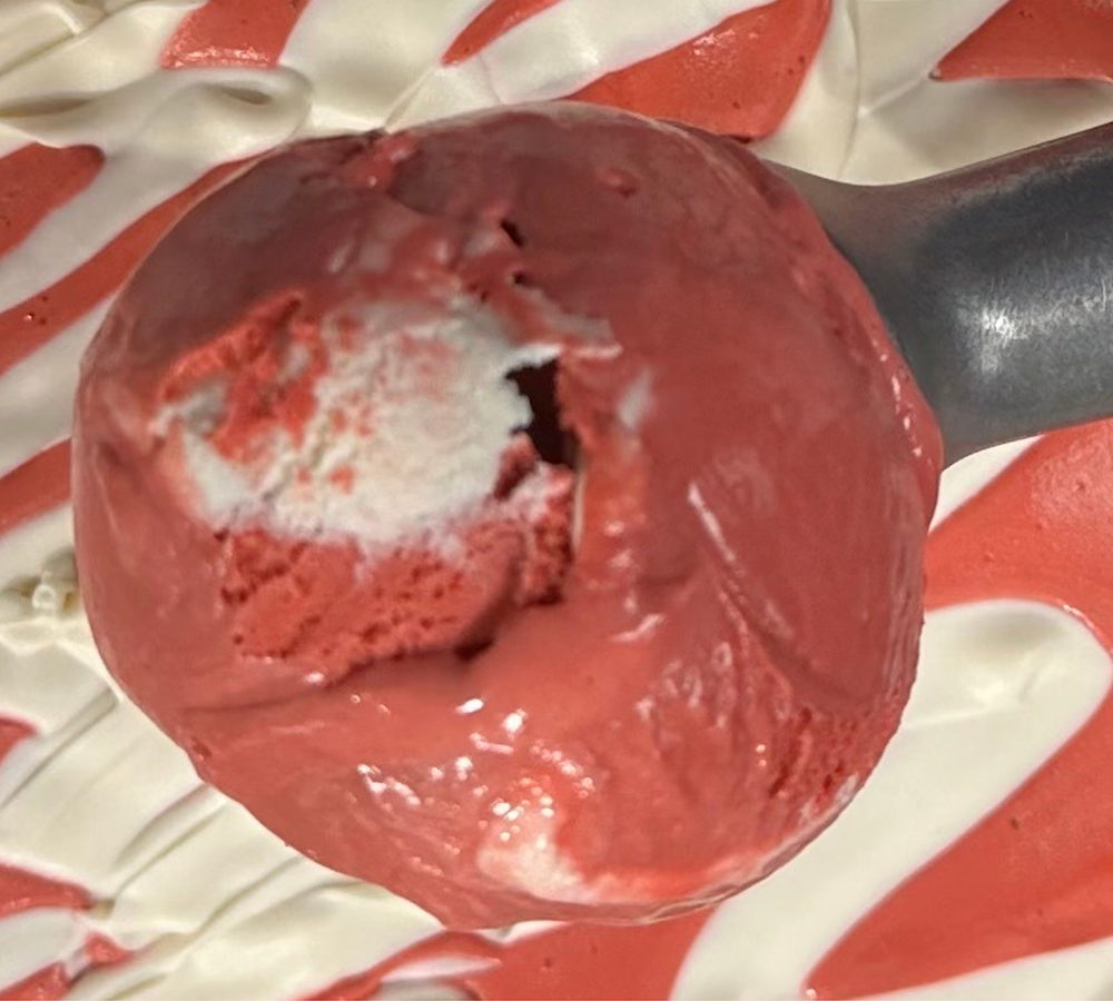 A person is holding an ice cream cone in front of a candy shelf.