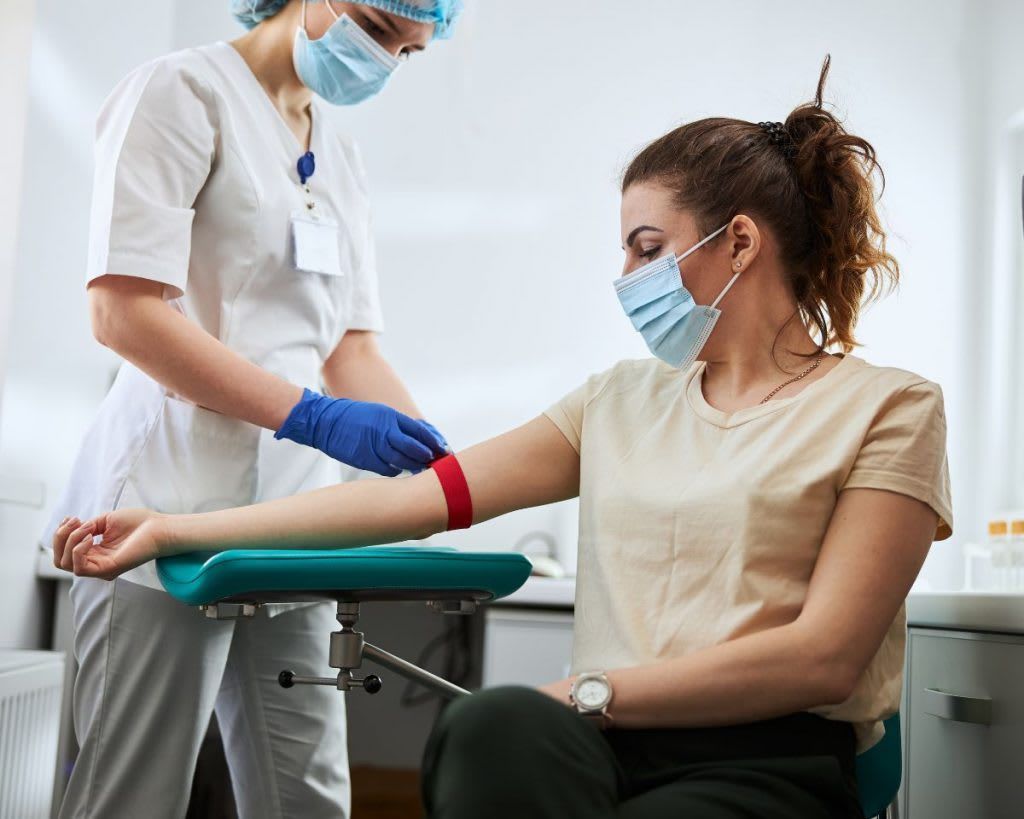 Medical professional applying tourniquet to a patient's arm for a blood draw in a clinic.