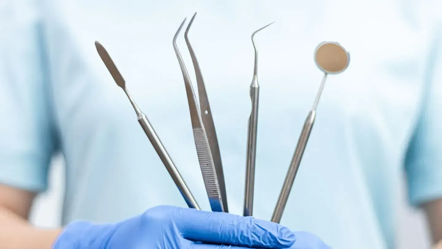 A dentist is holding a bunch of dental instruments in his hand.