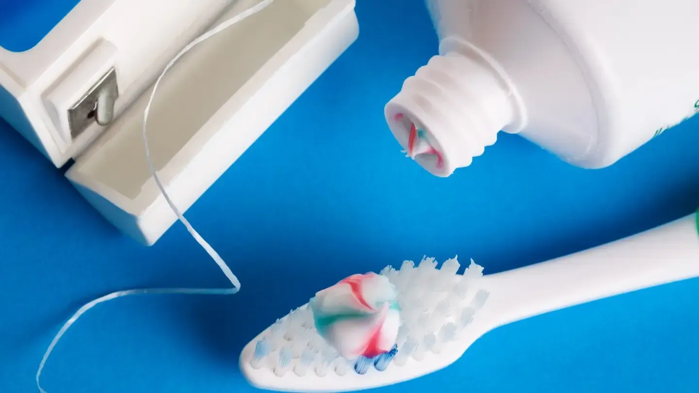 Toothbrush with toothpaste, dental floss, and a tube of toothpaste on a blue surface; dental hygiene items.