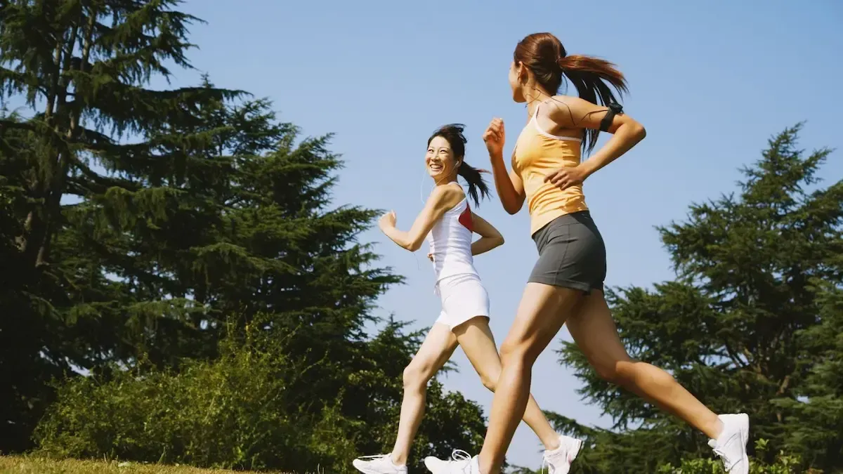 Two women running outdoors on a sunny day near trees.