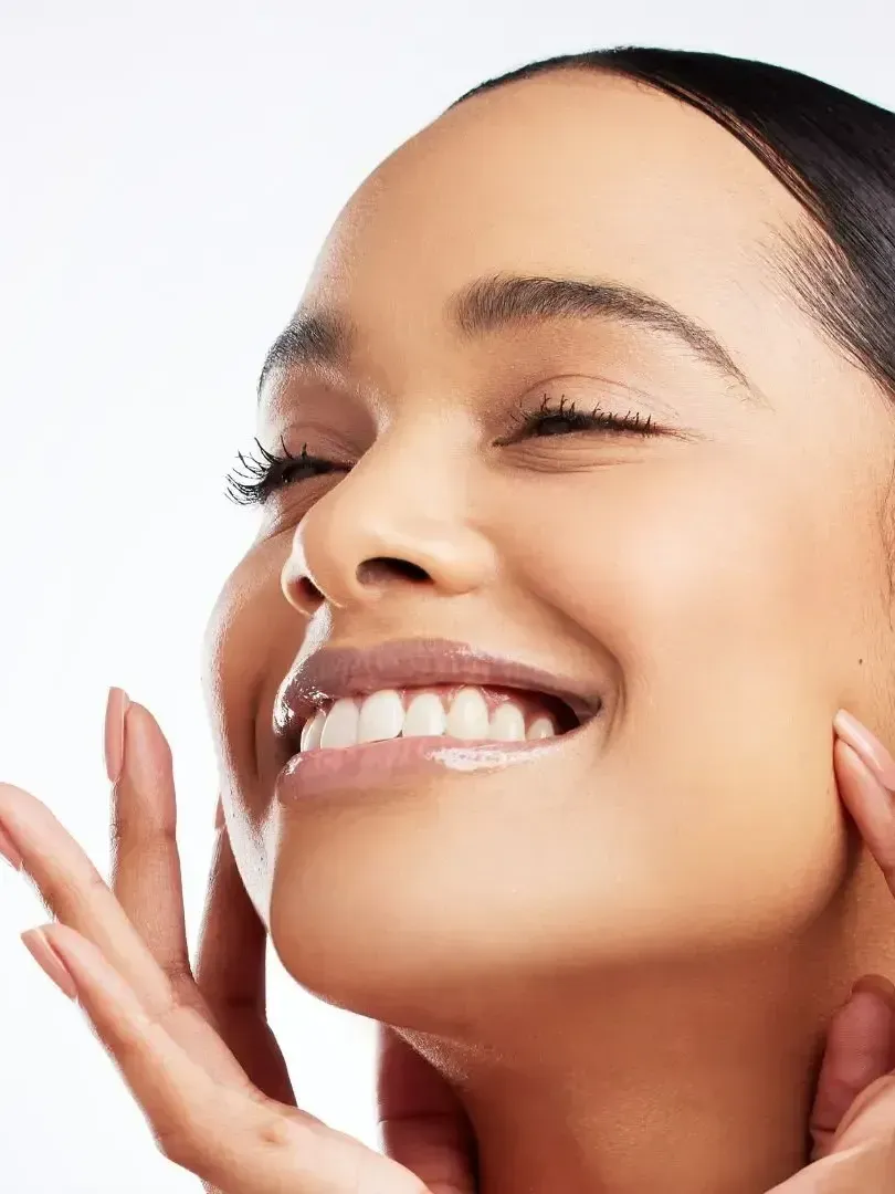A woman is smiling and touching her face with her hands
