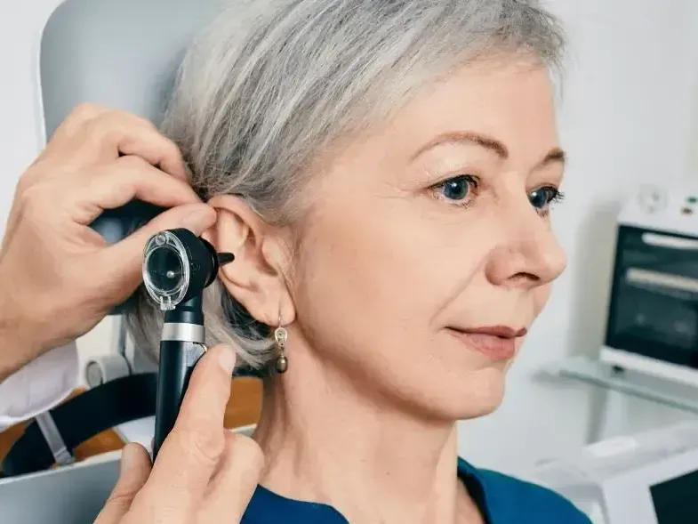 Doctor examining a person's ear with an otoscope in a medical setting.