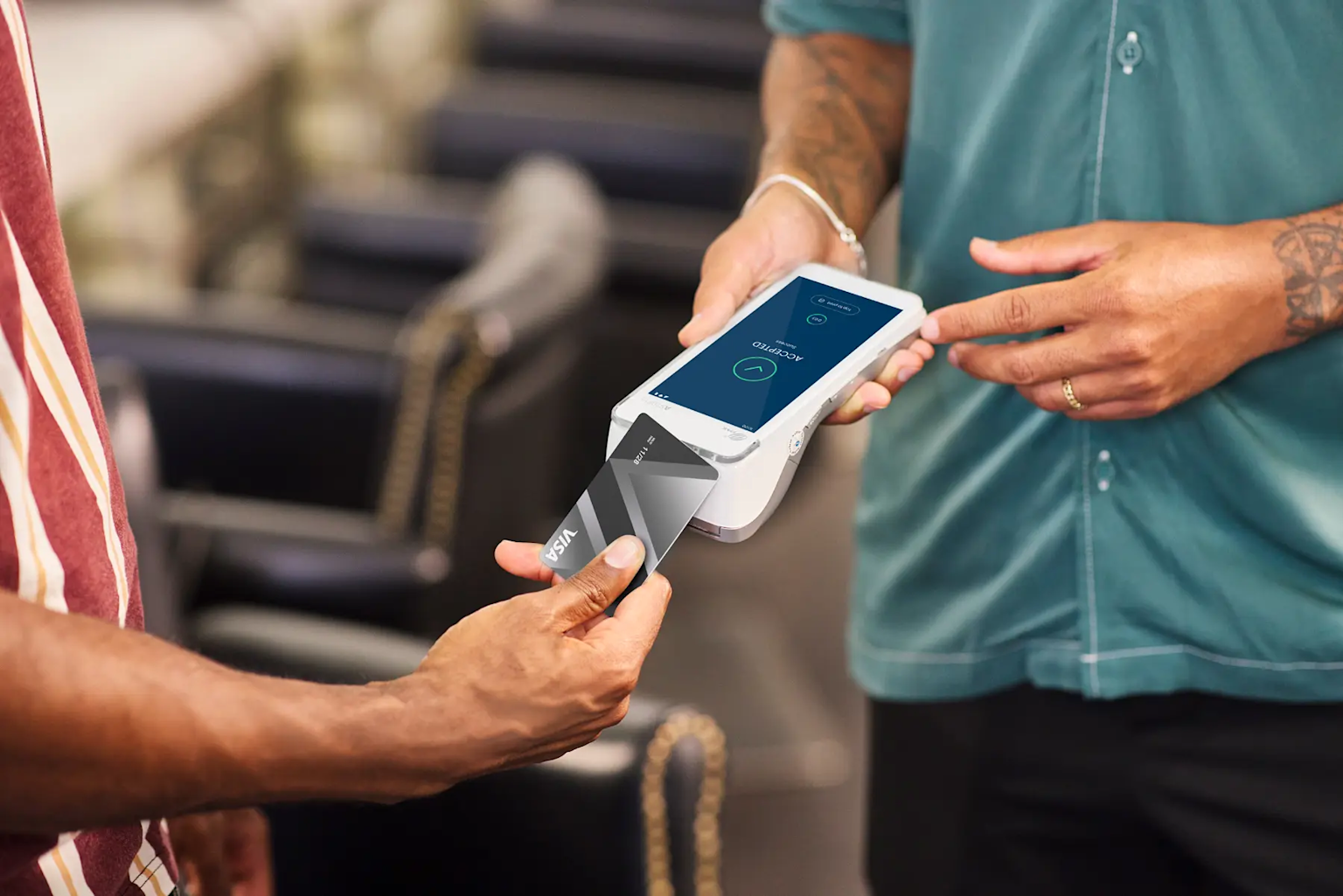 Person paying with a credit card at a point-of-sale device in a barbershop.
