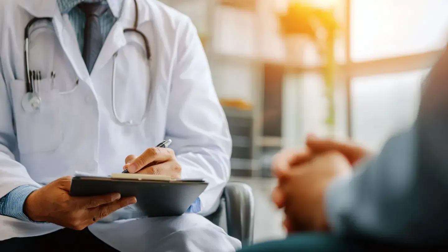 Doctor in white coat showing medication to patient on a sofa.