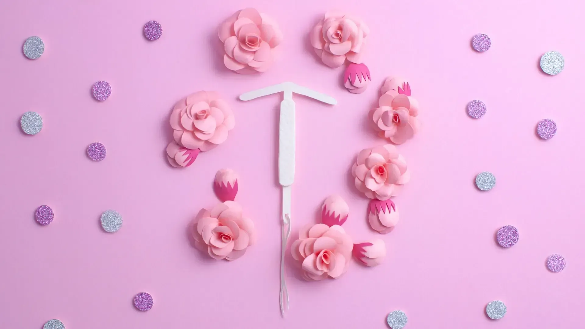 Pink background with a white IUD surrounded by pink flowers and confetti.
