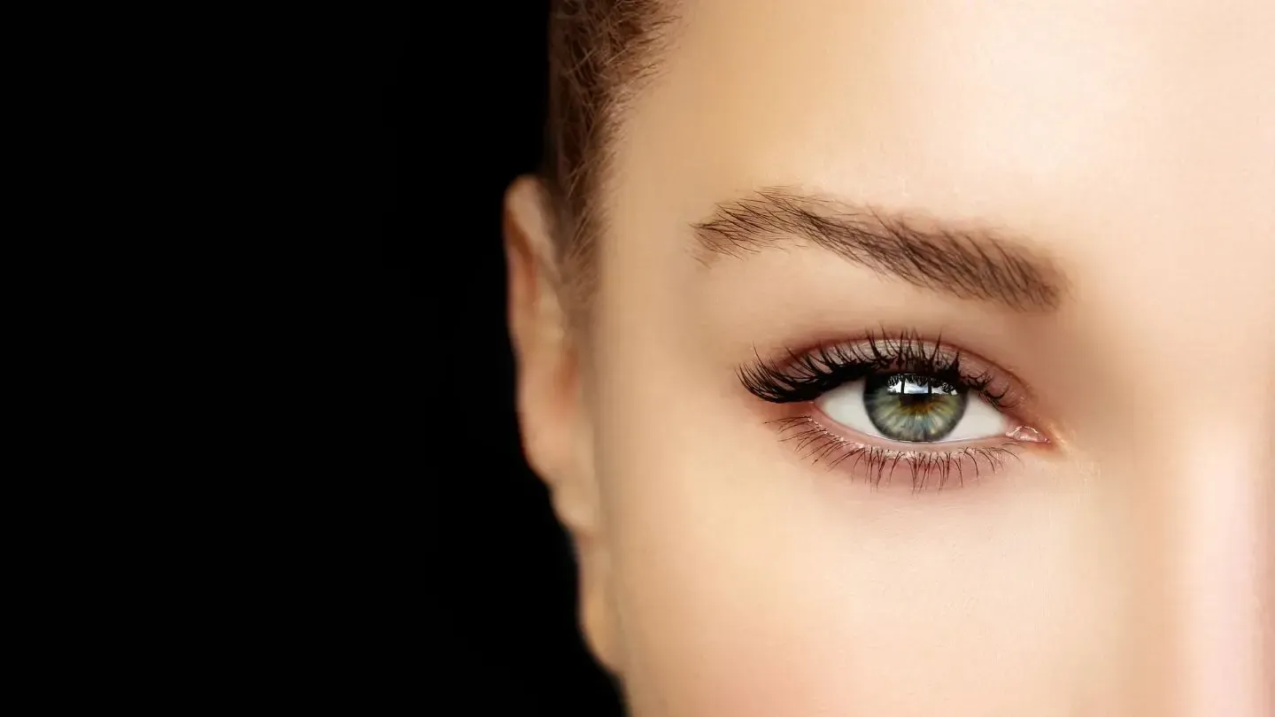 Close-up of a woman's eye with dark lashes and a green iris, against a black background.