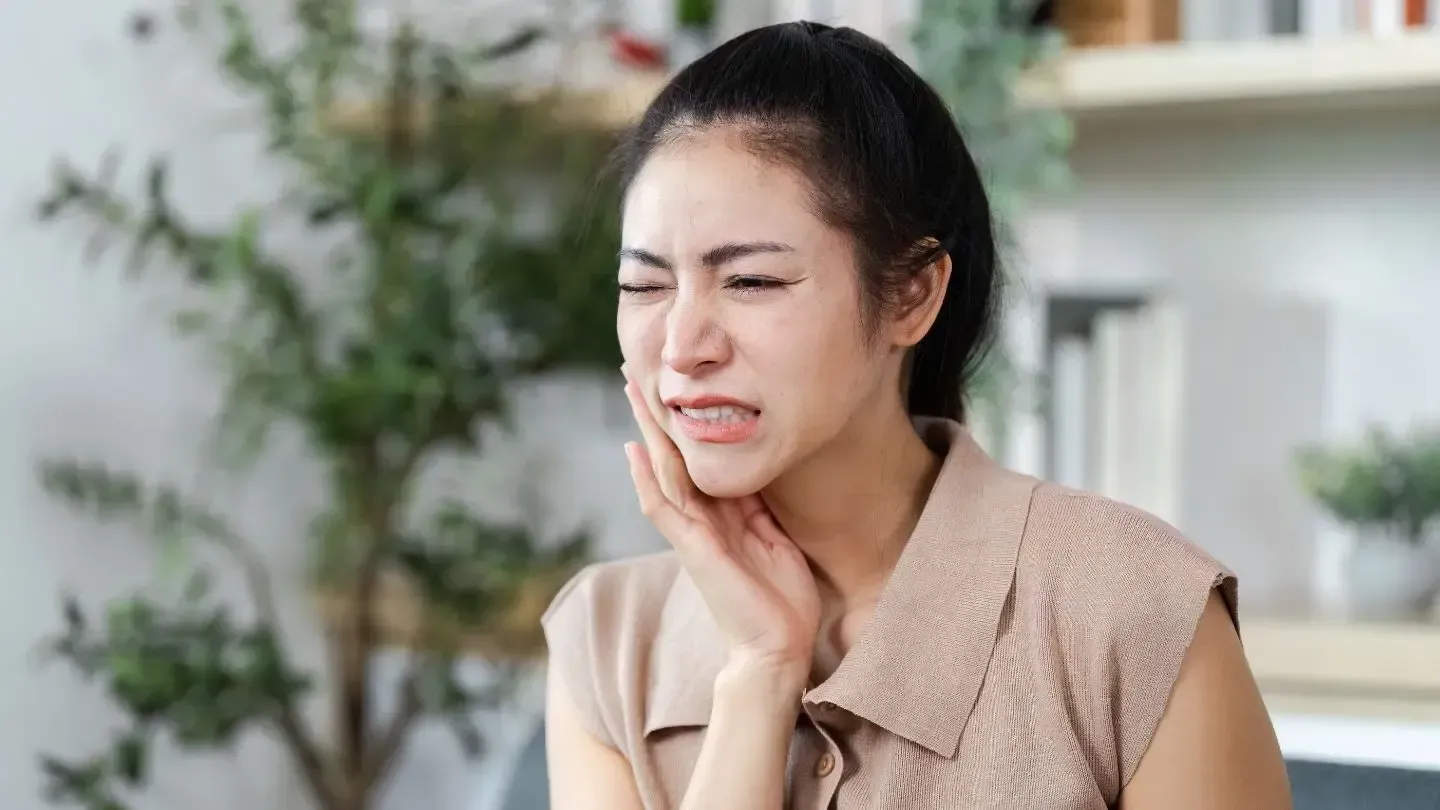 Woman clutching jaw, grimacing in pain indoors.