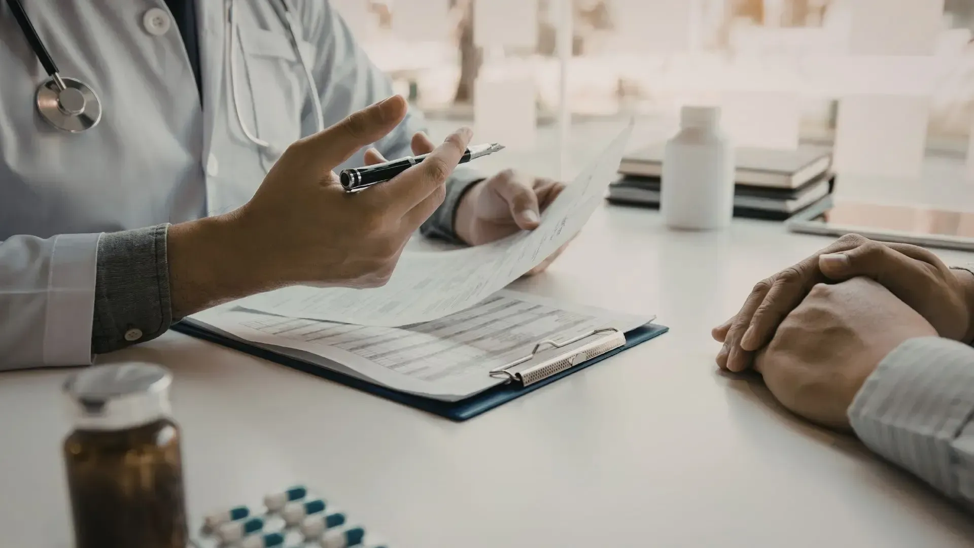 Doctor in white coat reviews paperwork with a patient at a desk.