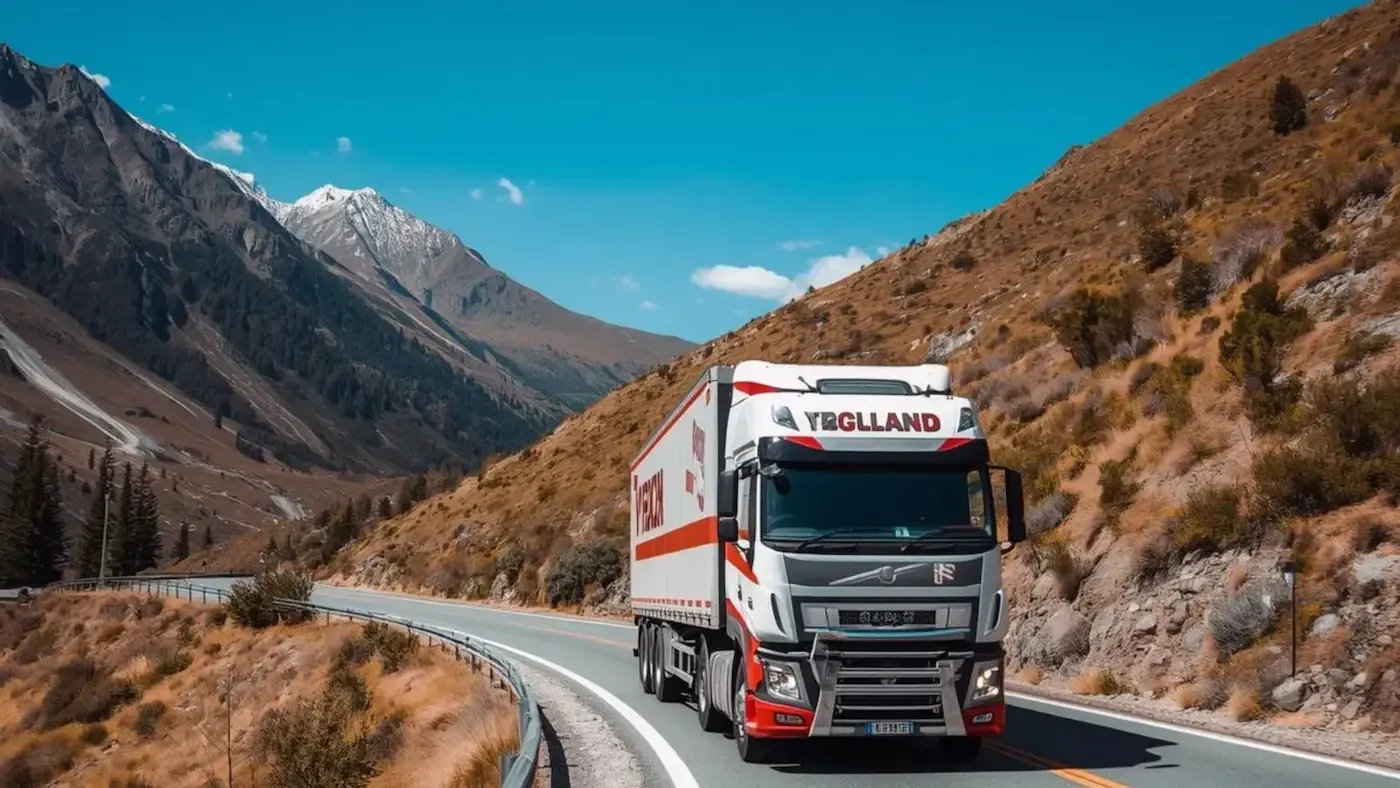 Truck driving on a winding road through mountains under a blue sky.