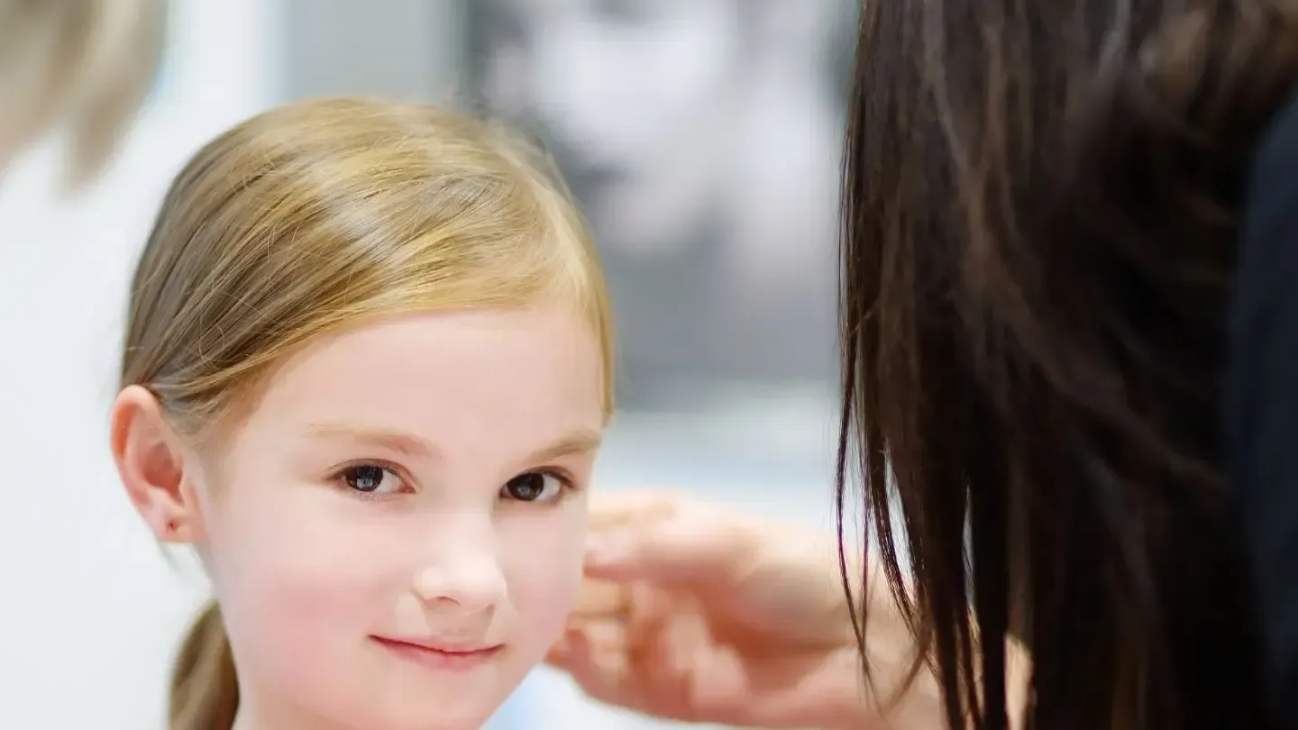 Girl with blonde hair getting her ear pierced by another person.