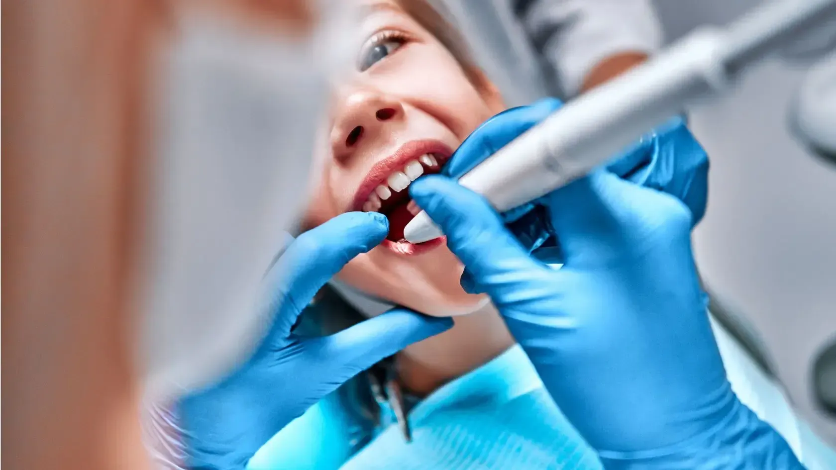 Child receiving dental treatment, dentist's gloved hands holding tools, blue gloves, focused, close-up shot.