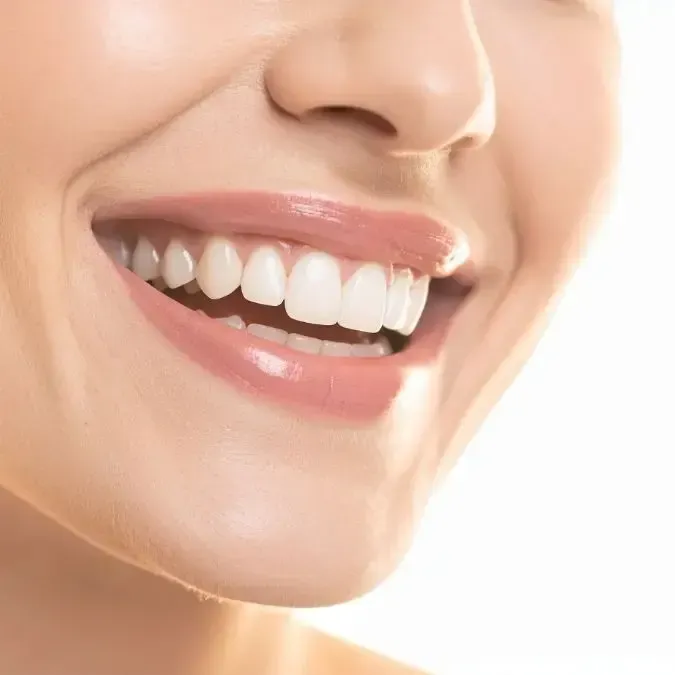 Close-up of a person smiling, showing white teeth and glossy pink lips.
