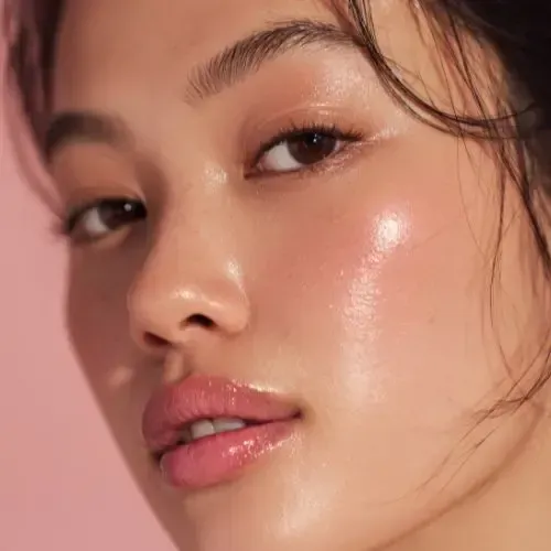 Close-up of a person with glossy skin and rosy cheeks, lips, and eyeshadow.
