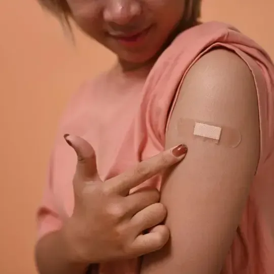 A woman in a pink shirt has a bandage on her arm