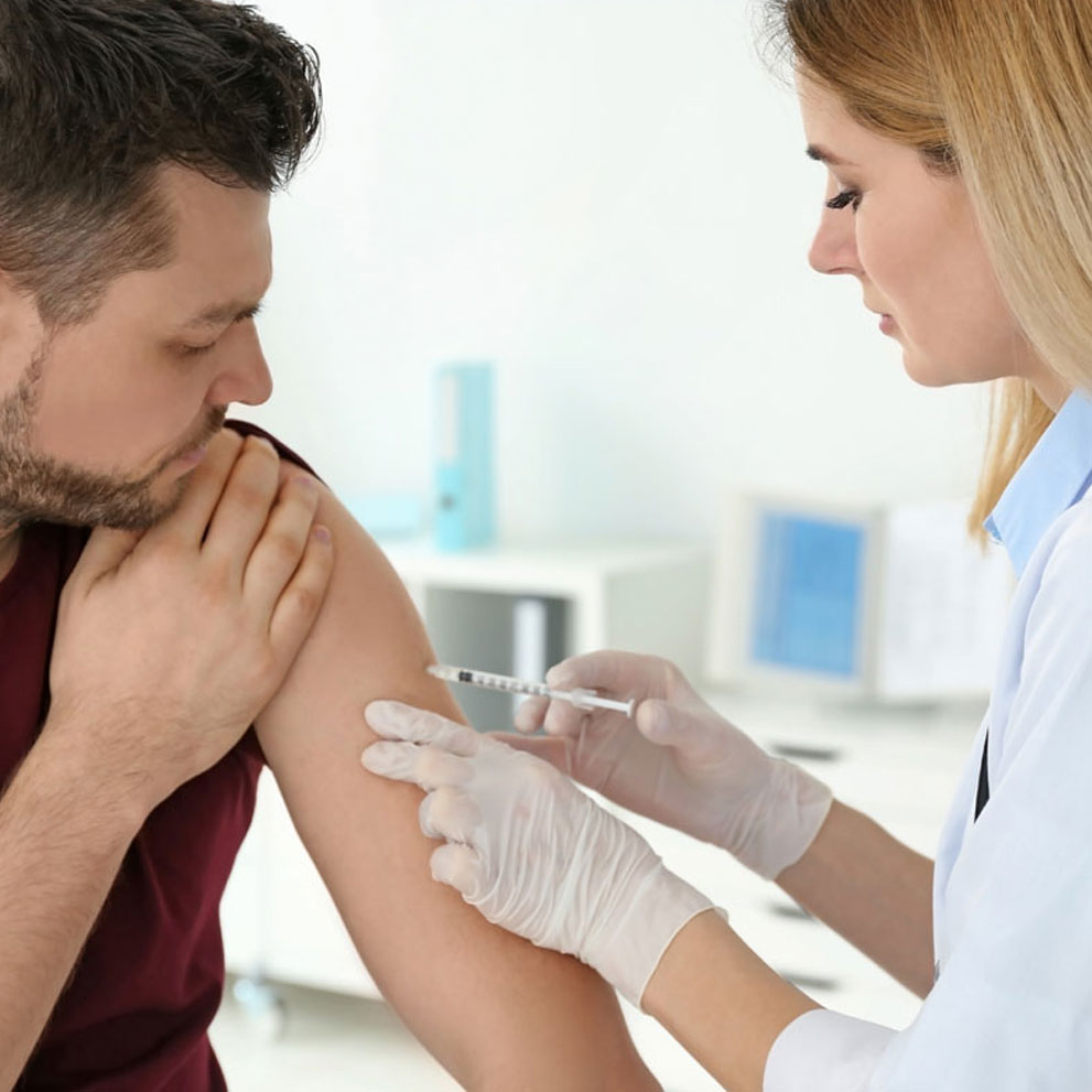 A person receiving a shot in their arm from a healthcare worker in a medical setting.