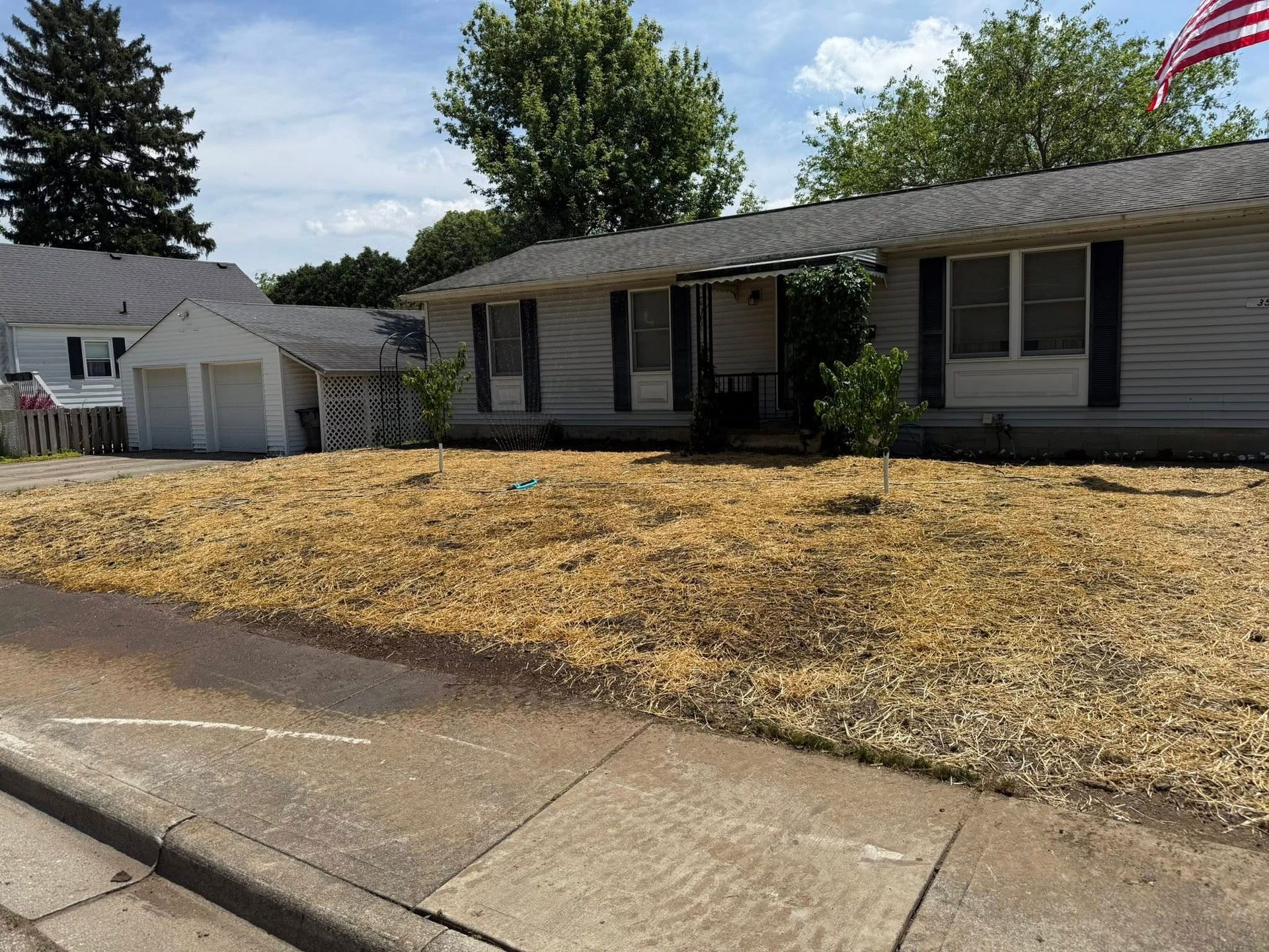 Ranch-style house with dry grass yard and detached garage, under a partly cloudy sky.