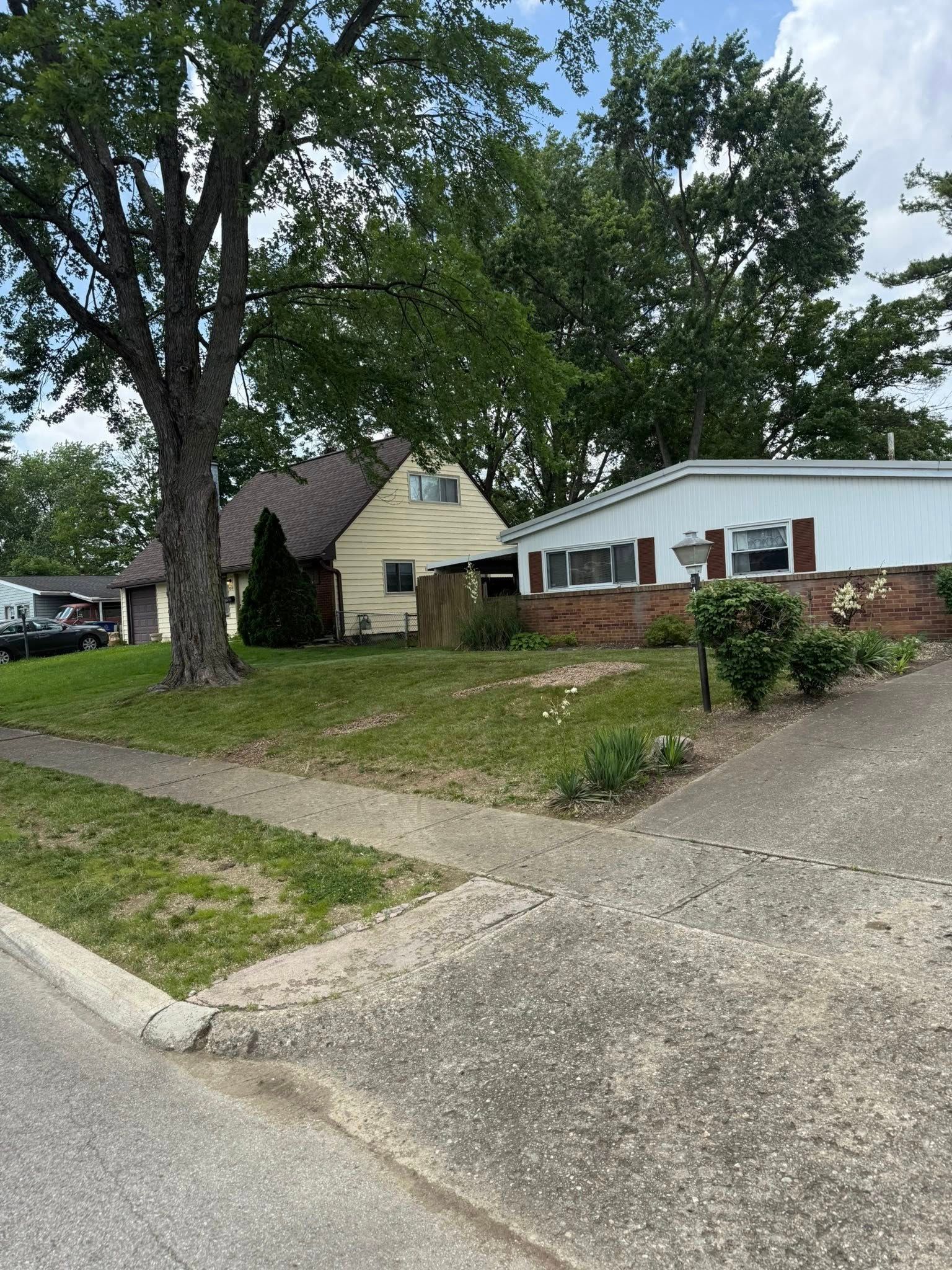 Houses with trees and grassy yards viewed from a sidewalk.