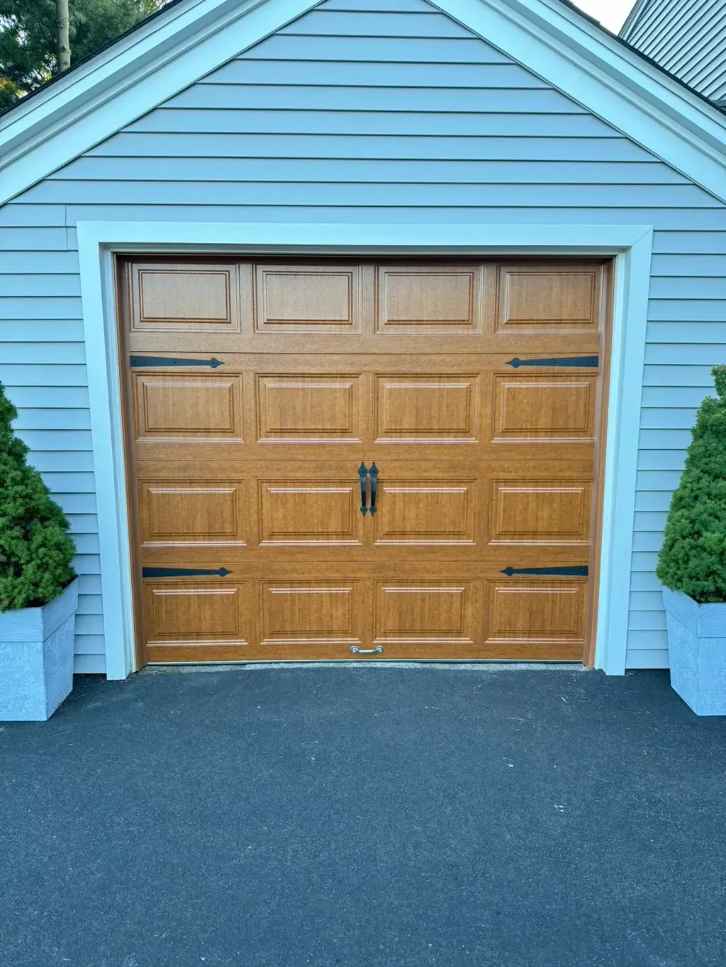 Brown garage door with black hardware in front of a light blue house.