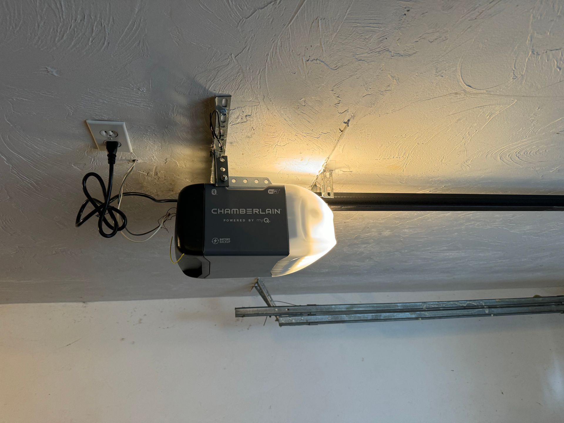 Garage door opener attached to ceiling. Black and silver unit with light on.
