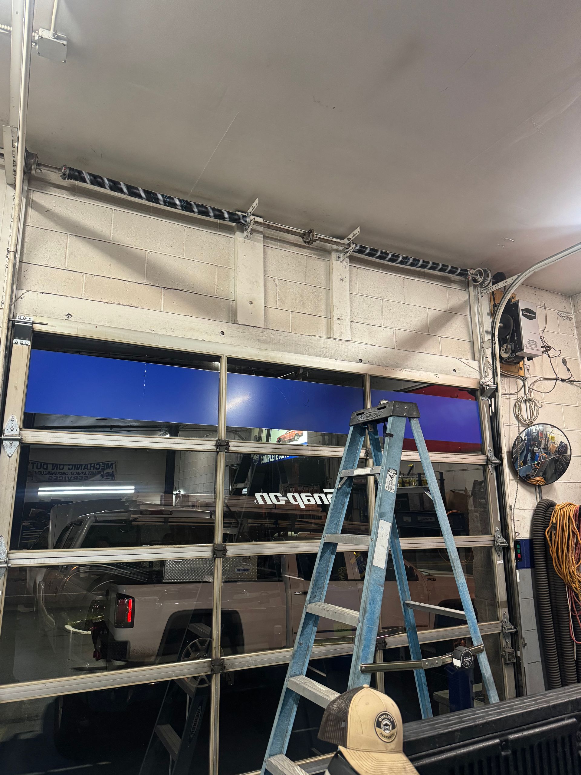 A garage door with blue tinted glass panels is partially open, a ladder inside.