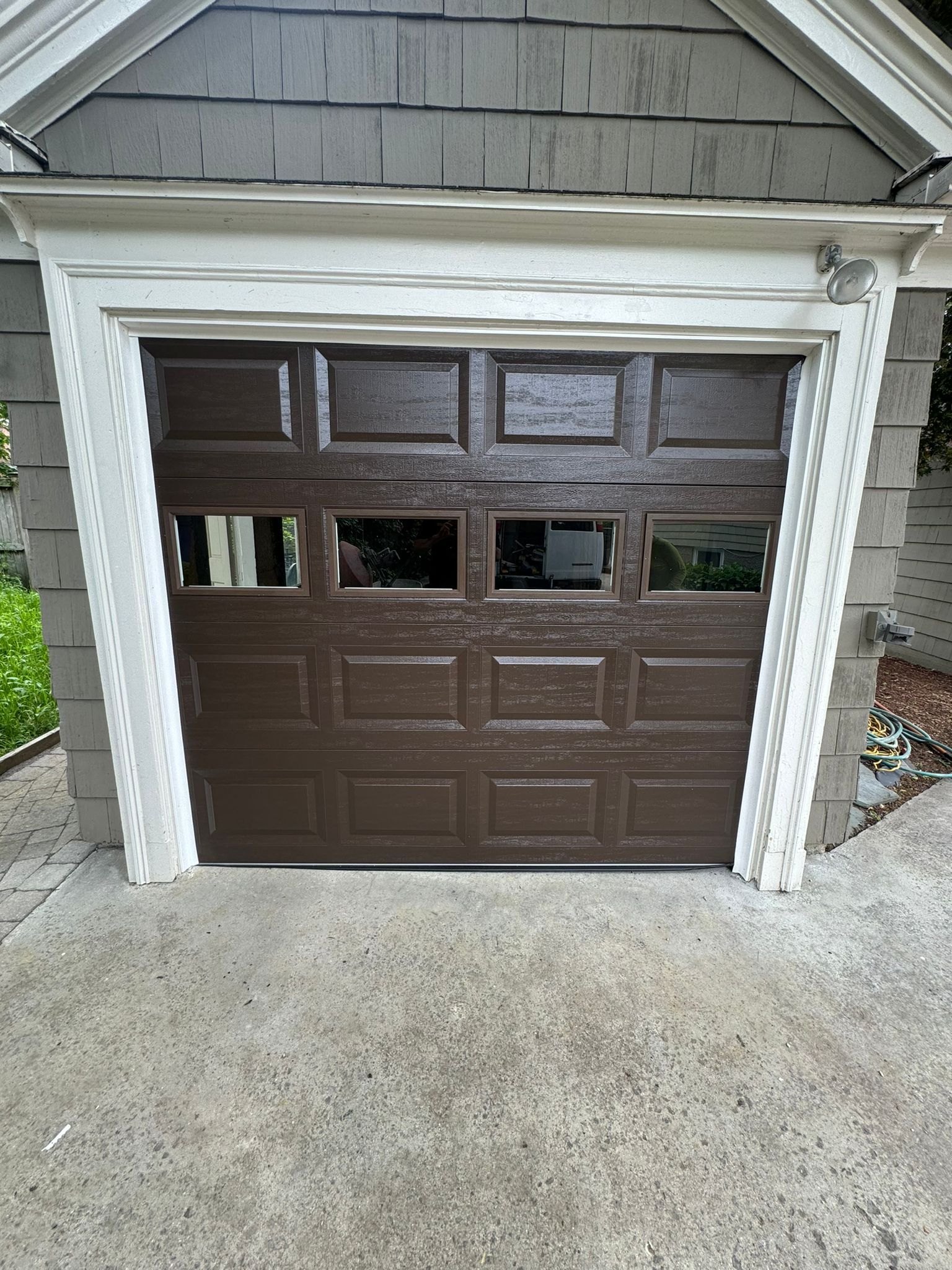 Brown garage door with windows, white trim, gray siding, and concrete driveway.