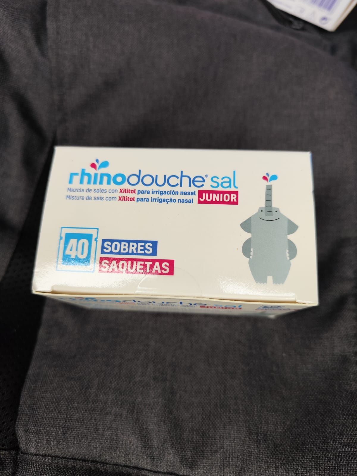 Caja de sobres de Rhinodouche sal Junior sobre una superficie de tela oscura, con la ilustración de un rinoceronte gris.