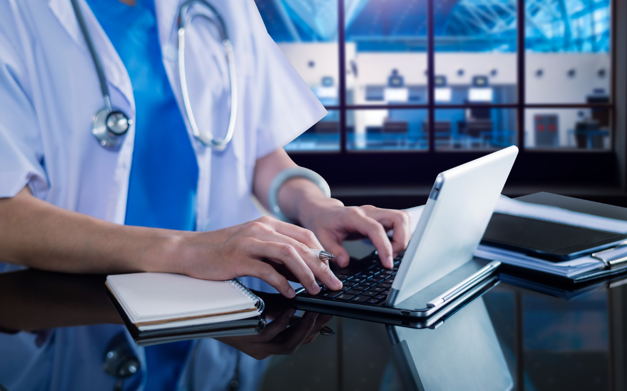 A doctor is typing on a laptop computer at a desk.
