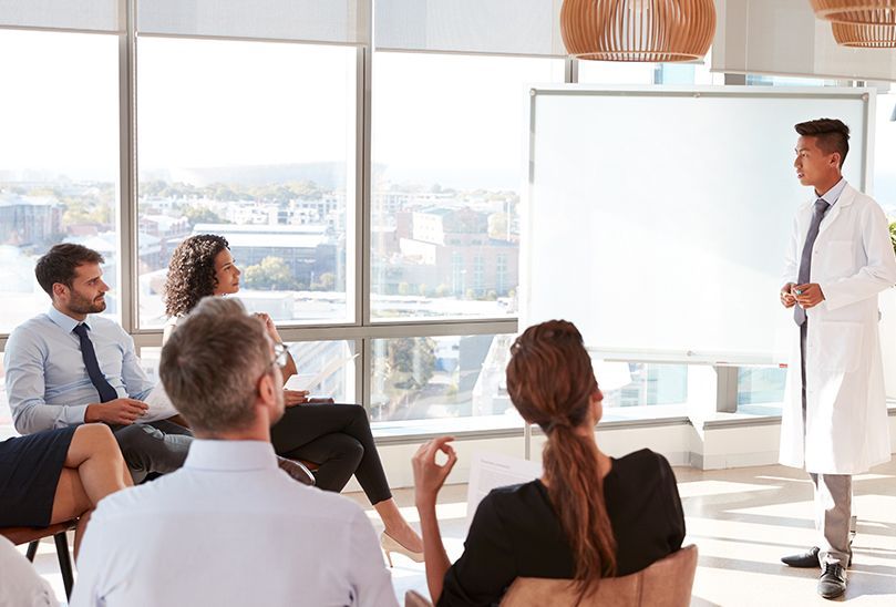 A man in a lab coat is giving a presentation to a group of people.