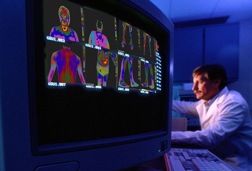 A man in a lab coat is looking at images on a computer screen