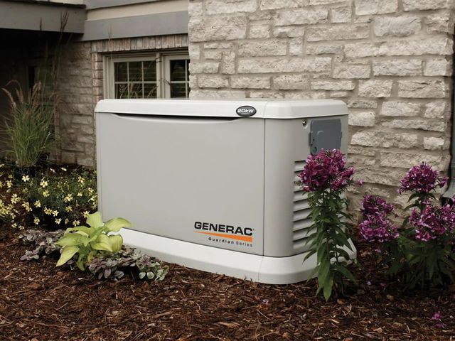 Generator, gray casing, on gravel base, near brick wall. Gas pipes connected.